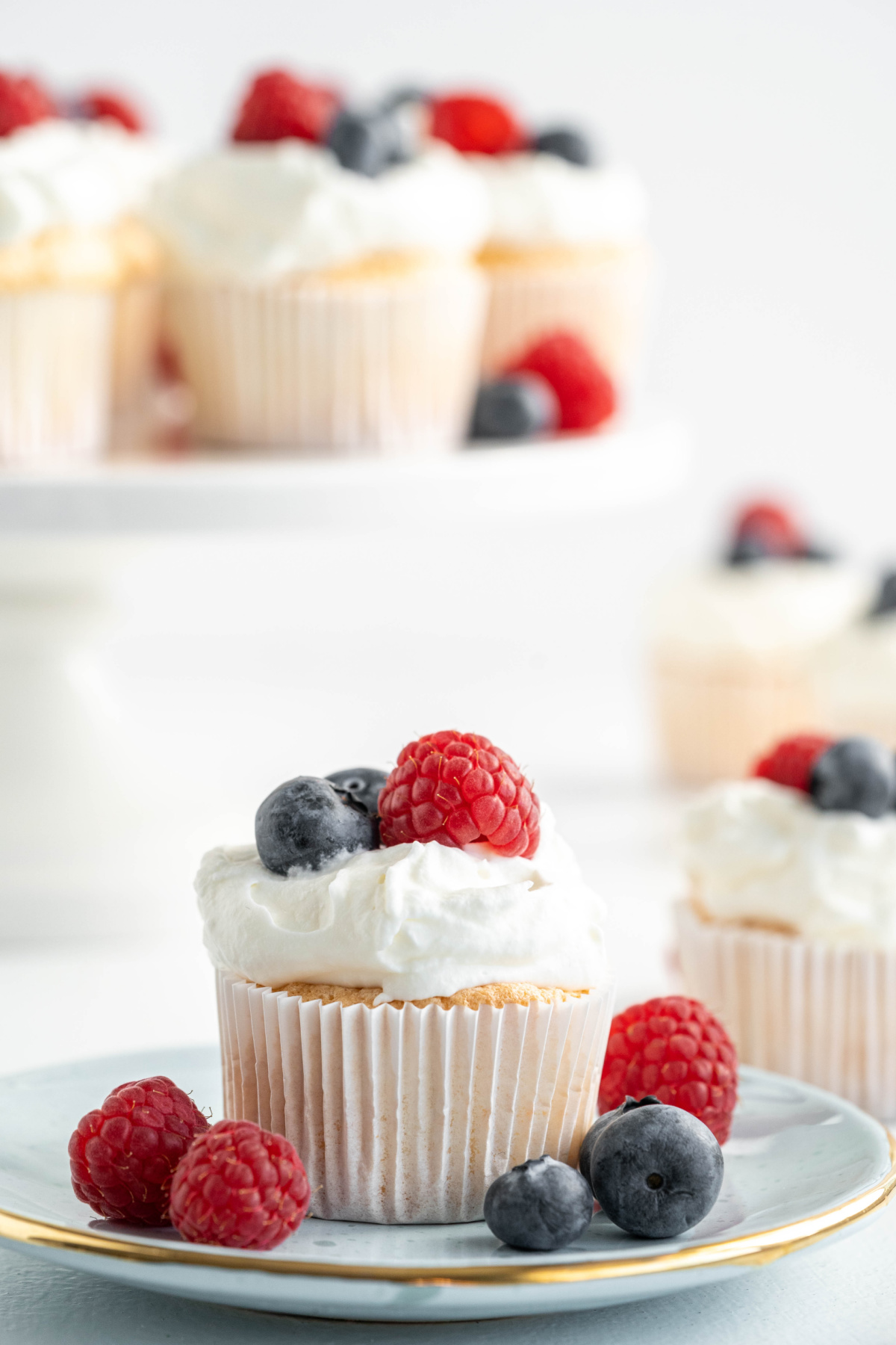 Angel food cupcake topped with homemade whipped cream, raspberries, and blueberries on a dessert plate