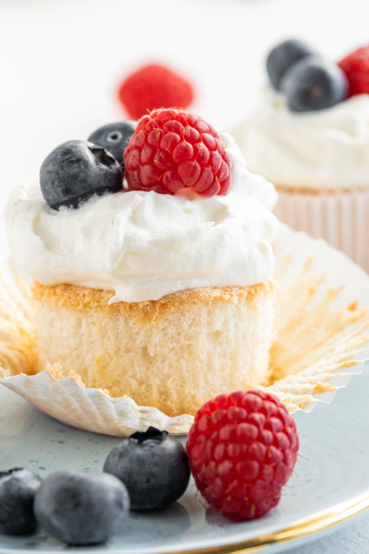 Inside of an angel food cupcake showing the light, airy texture beneath whipped cream and fresh berries