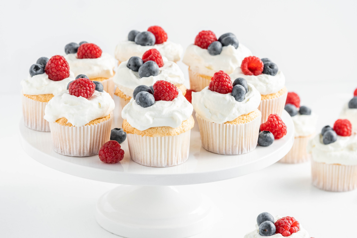 Angel food cupcakes with homemade whipped cream and fresh berries arranged on a white cake stand