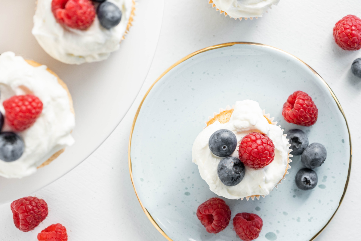 Overhead view of angel food cupcakes topped with homemade whipped cream, raspberries, and blueberries