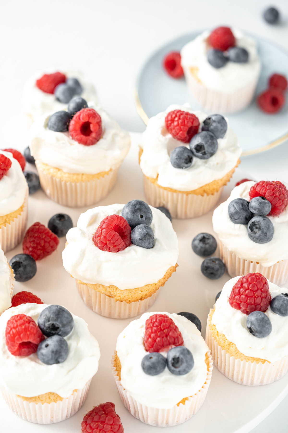 Angel food cupcakes topped with homemade whipped cream, raspberries, and blueberries