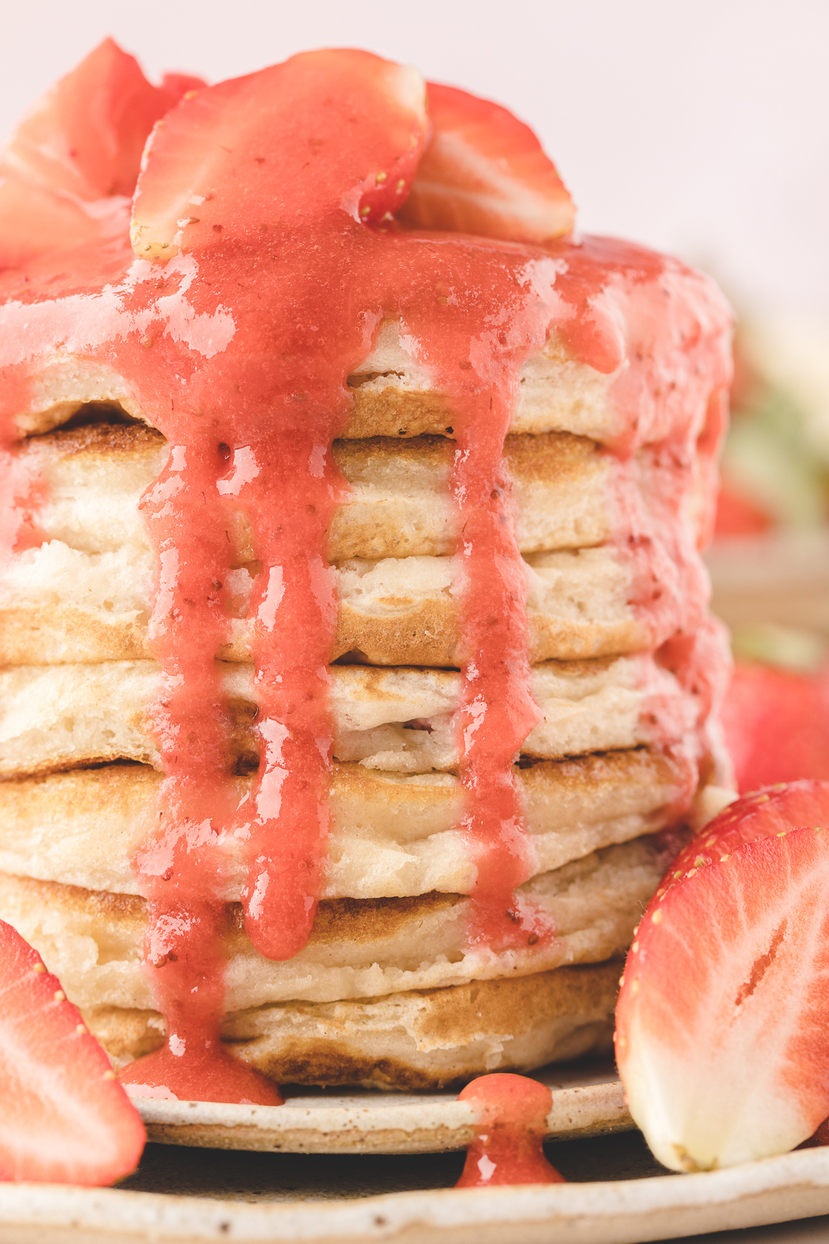 Fresh strawberry buttermilk pancakes stacked high with glossy strawberry sauce dripping down the sides and fresh strawberries around the plate.