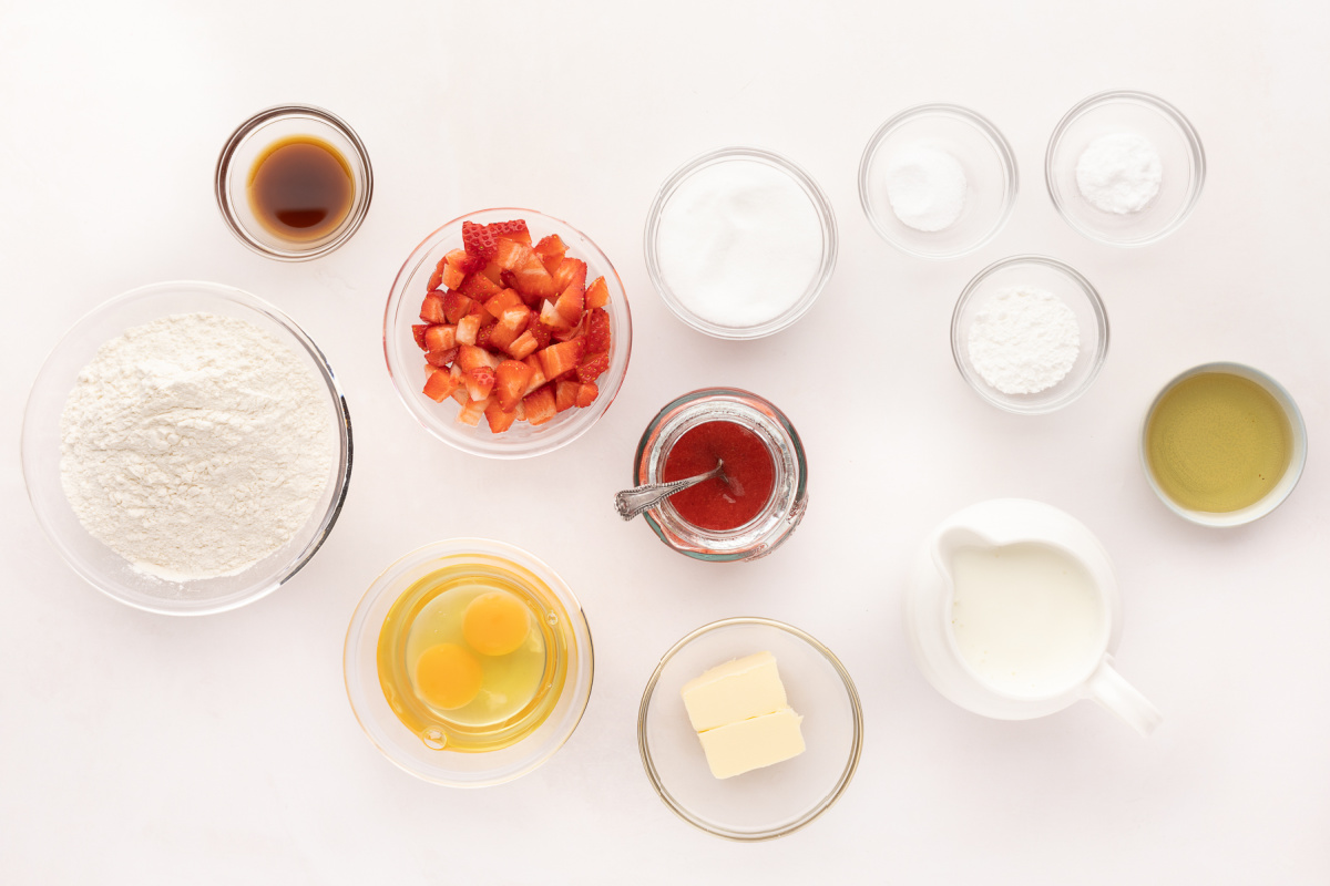 Ingredients for fresh strawberry pancakes including buttermilk, chopped strawberries, flour, eggs, butter, vanilla, and strawberry sauce.