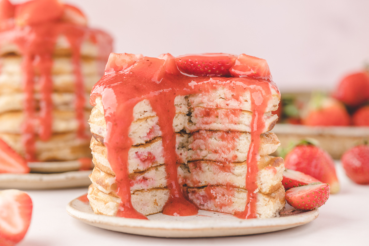 Fresh strawberry pancakes sliced open to show jammy strawberry pockets inside the buttermilk pancake stack with warm strawberry sauce poured over the top.