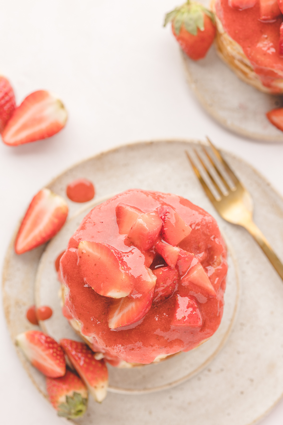 Overhead view of strawberry pancakes covered in warm strawberry sauce and topped with fresh sliced strawberries on a ceramic plate.