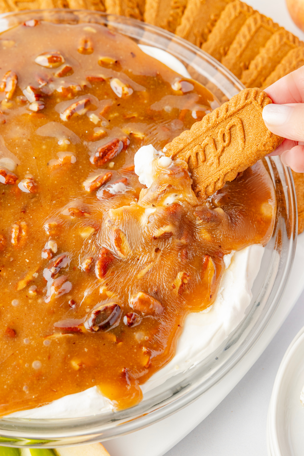Pecan pie dip being scooped with a Biscoff cookie, showing the warm caramel pecan topping pulling away from the cold cream cheese layer.
