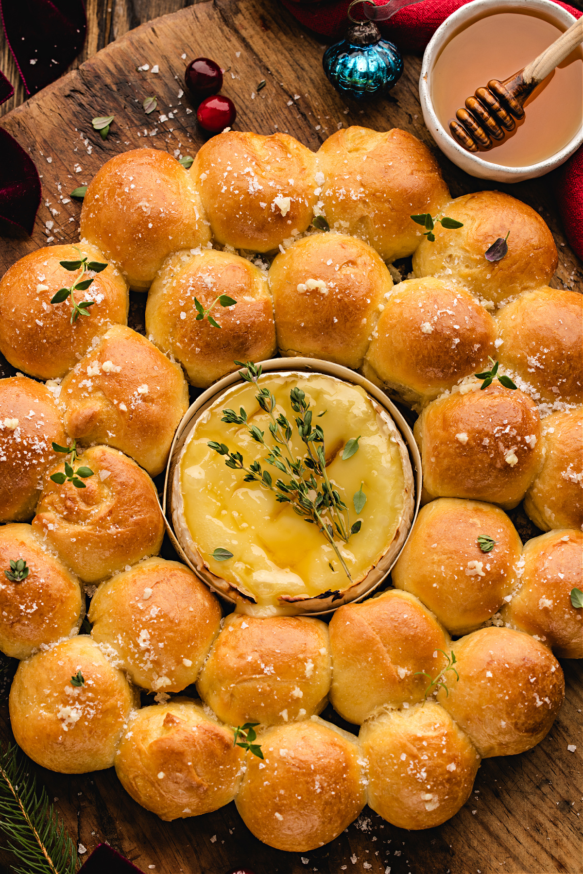 A warm baked Camembert wreath with golden rolls and a melted cheese center topped with honey and fresh thyme.