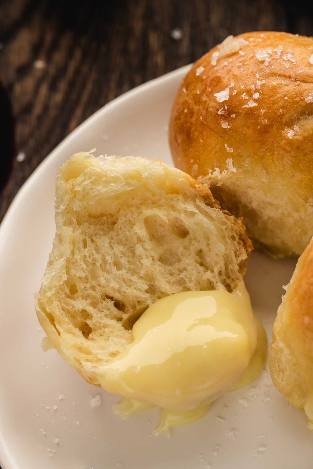 A torn bread roll on a white plate with melted Camembert oozing from the center.