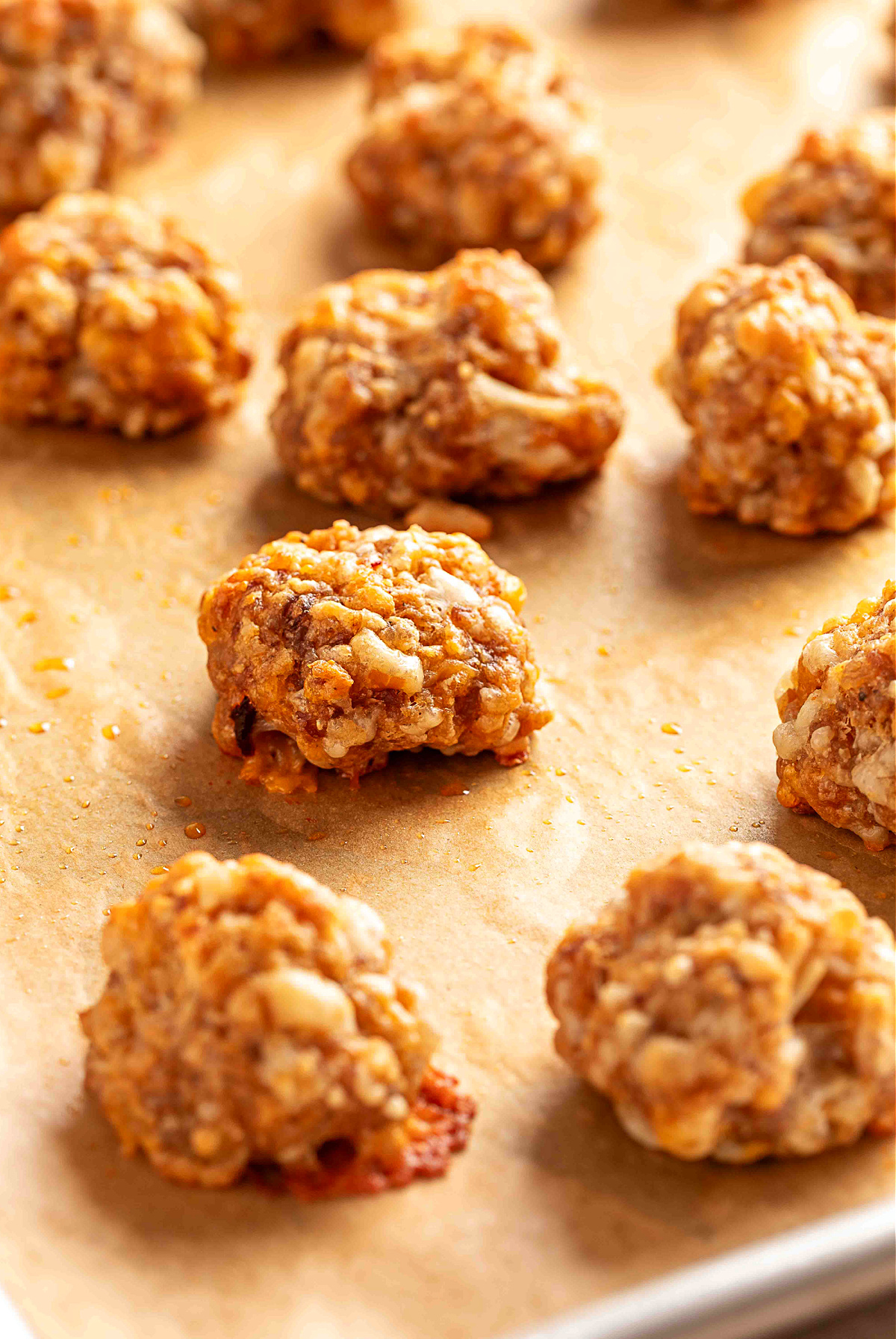 Freshly baked sausage balls cooling on a parchment-lined sheet pan, showing their crisp golden edges and melted smoked cheddar pockets.