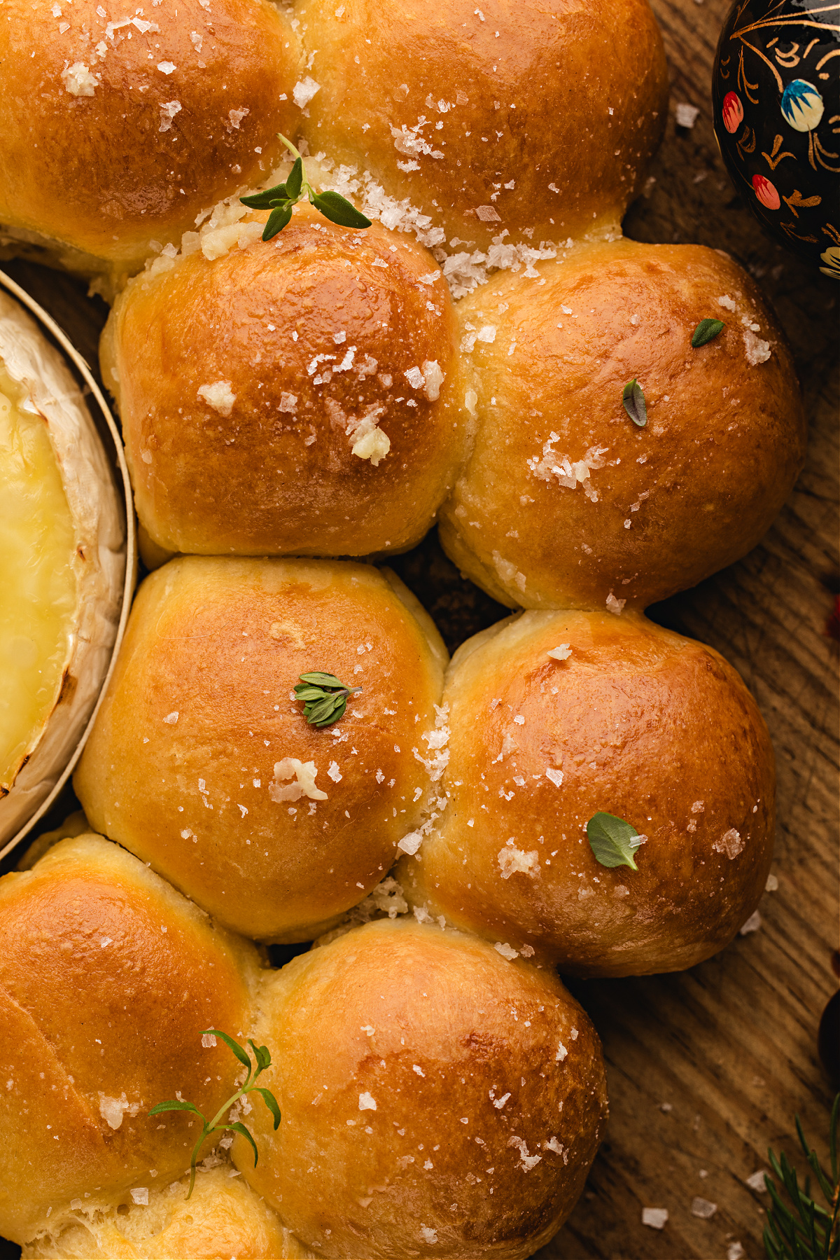 A close-up of the golden dinner rolls in the wreath, topped with sea salt flakes and fresh thyme.