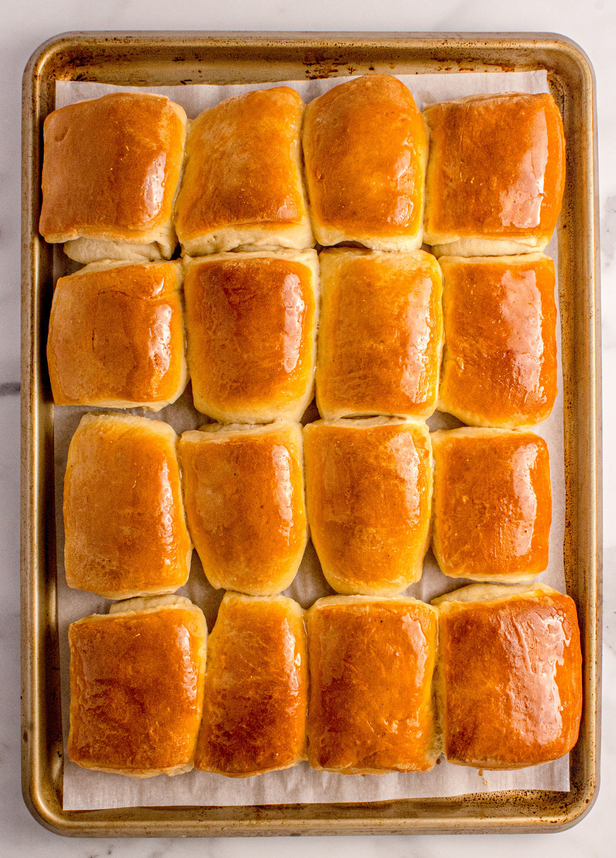 Soft Parker House Rolls brushed with butter on a baking sheet, classic folded yeast rolls made for holiday dinners, by Noble Pig.