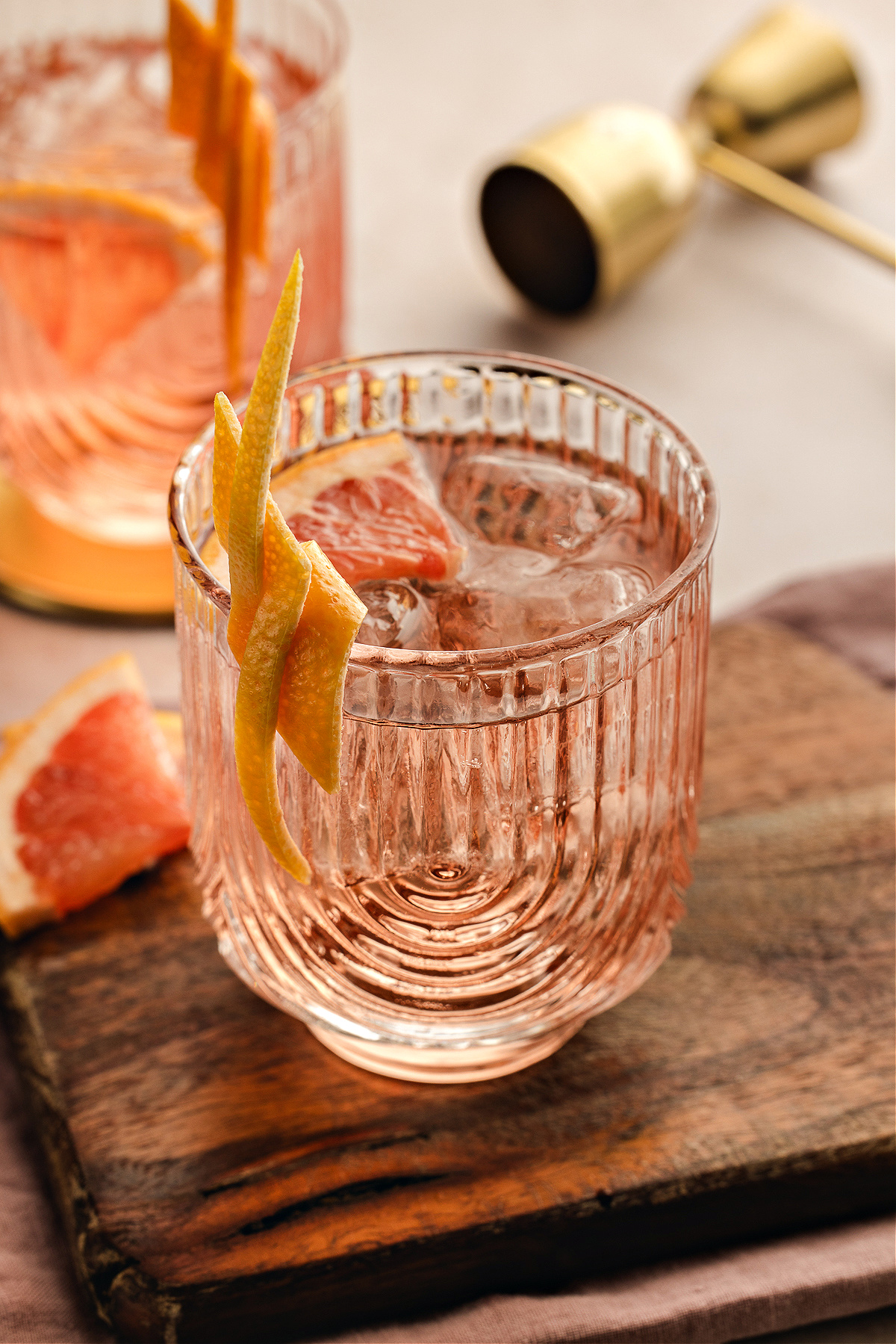 A pale pink Lillet Ros&eacute; spritz served over ice in a textured glass, finished with a long grapefruit twist and a slice tucked inside, with bar tools and another spritz blurred in the background.