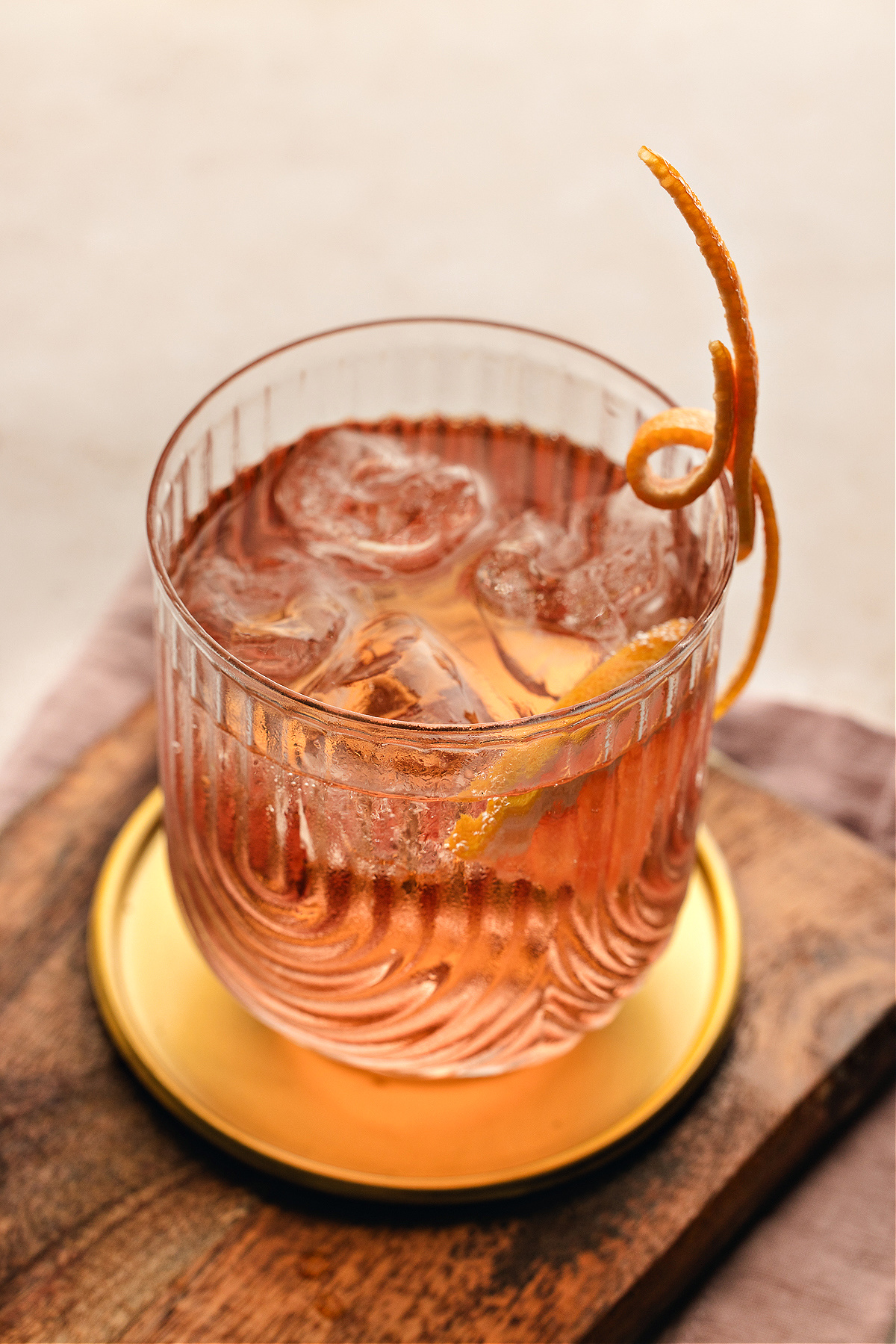 A chilled Lillet Ros&eacute; spritz glowing pale pink in a textured glass, served over ice with a long curled grapefruit twist resting on the rim.