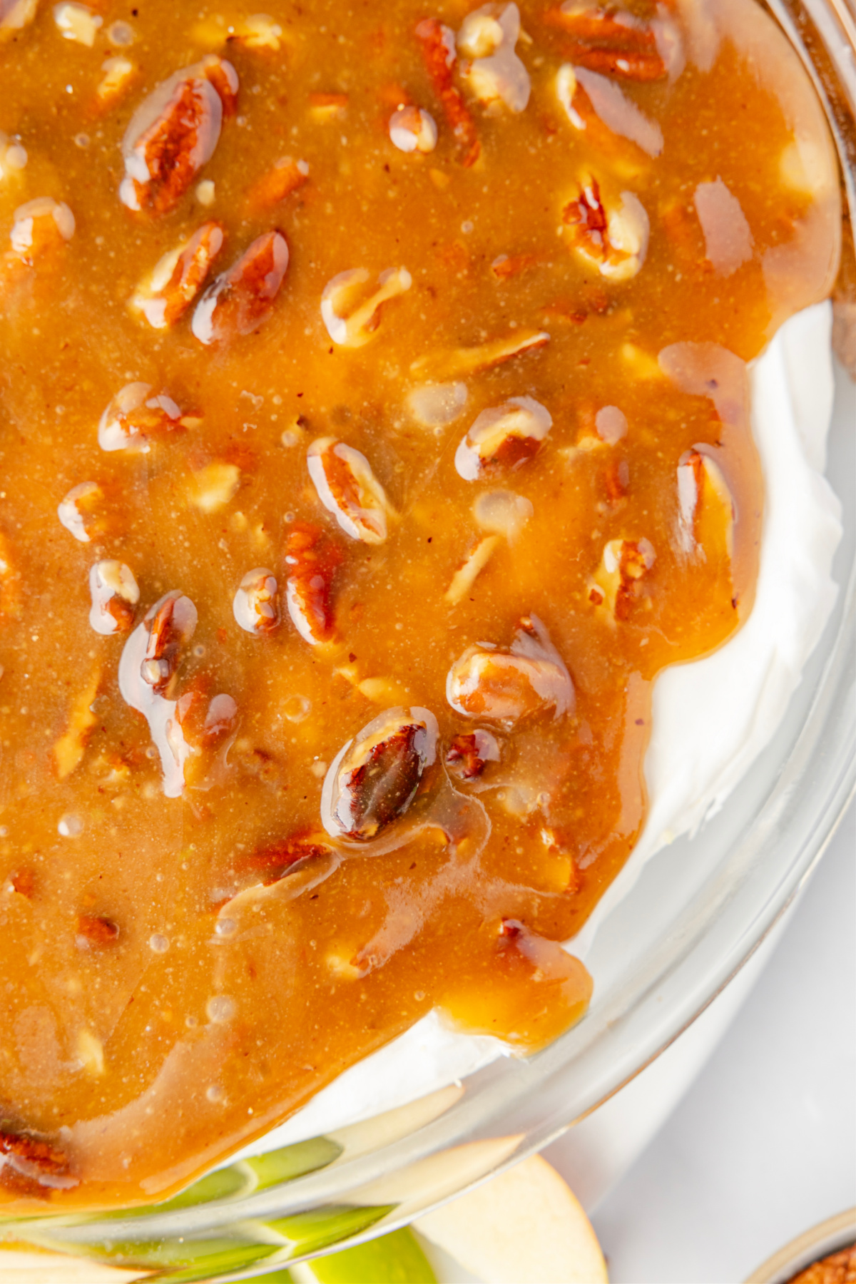 Close-up of pecan pie dip showing the warm caramel pecan topping over the cold cream cheese layer, highlighting the glossy brown sugar texture.