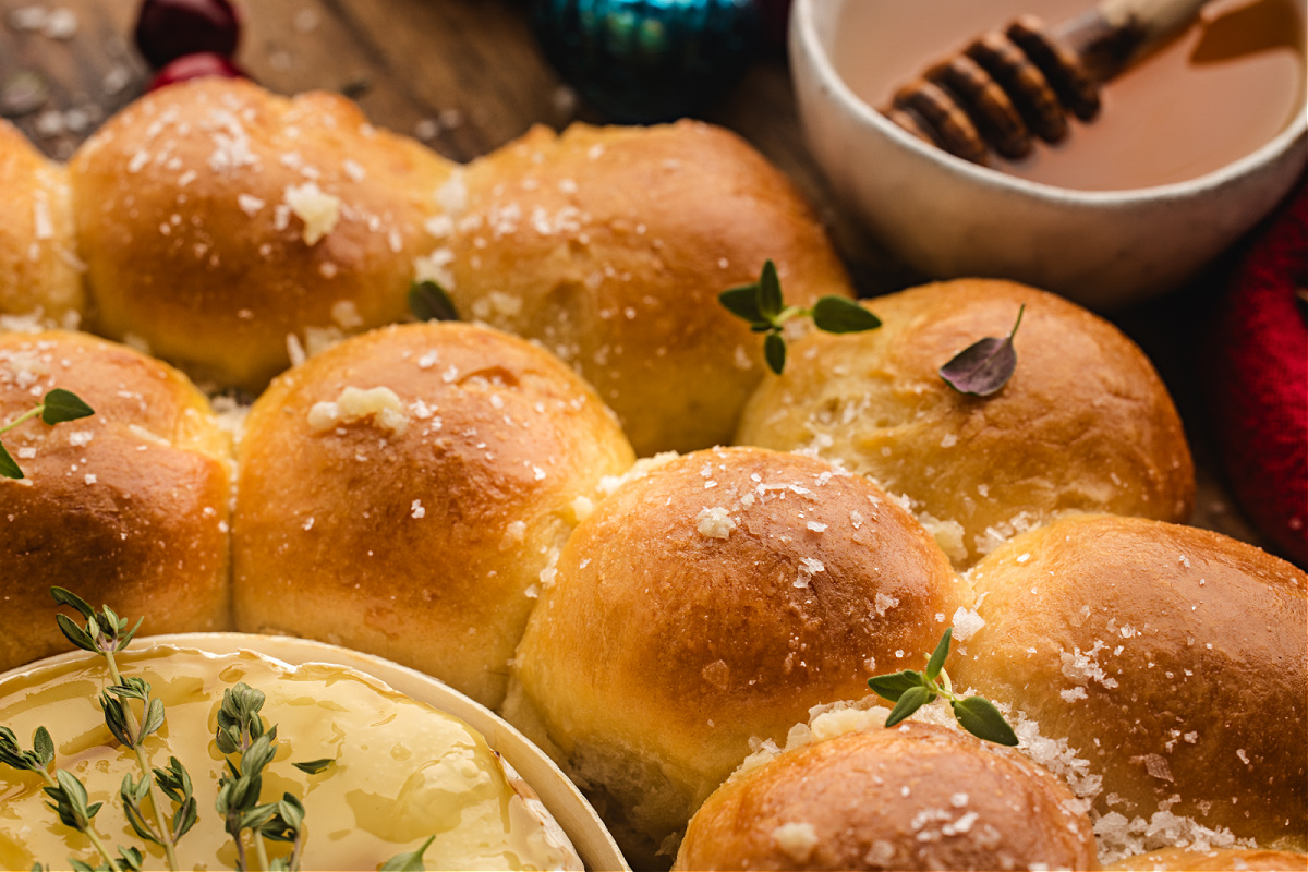 Golden pull-apart bread rolls sprinkled with sea salt and thyme, with a bowl of warm honey in the background.