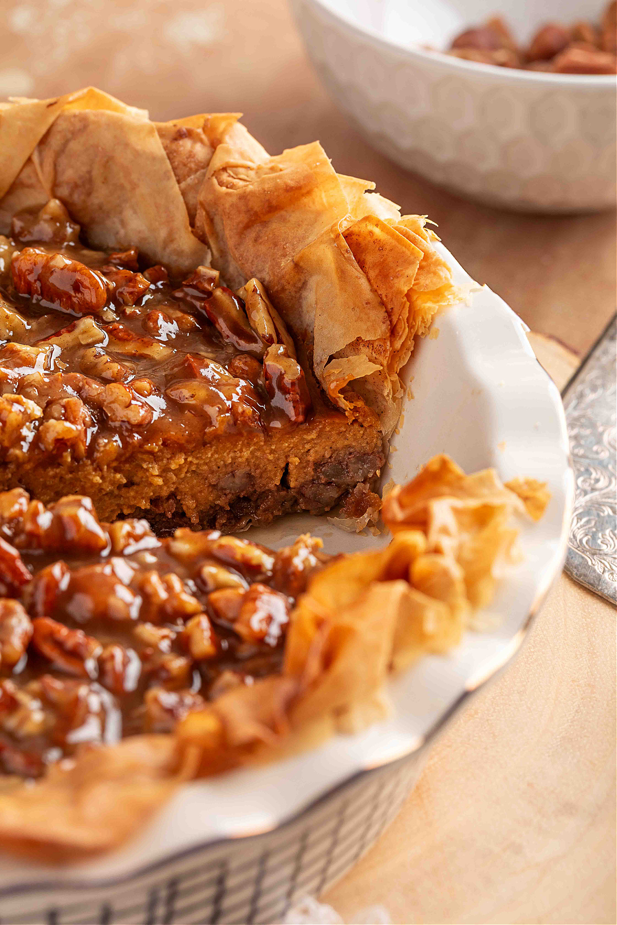 A sliced pumpkin praline pie with a ruffled phyllo crust, showing the layered bottom pecan-sugar base, the smooth pumpkin custard center, and the glossy pecan praline topping pooling over the cut edge.