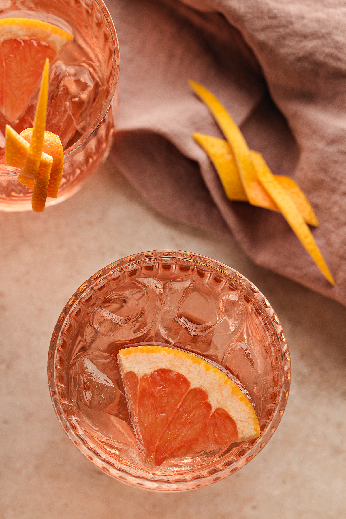 Two pale pink Lillet Ros&eacute; spritz cocktails viewed from above, each served over ice with fresh grapefruit and long citrus twists, set beside a soft mauve linen.