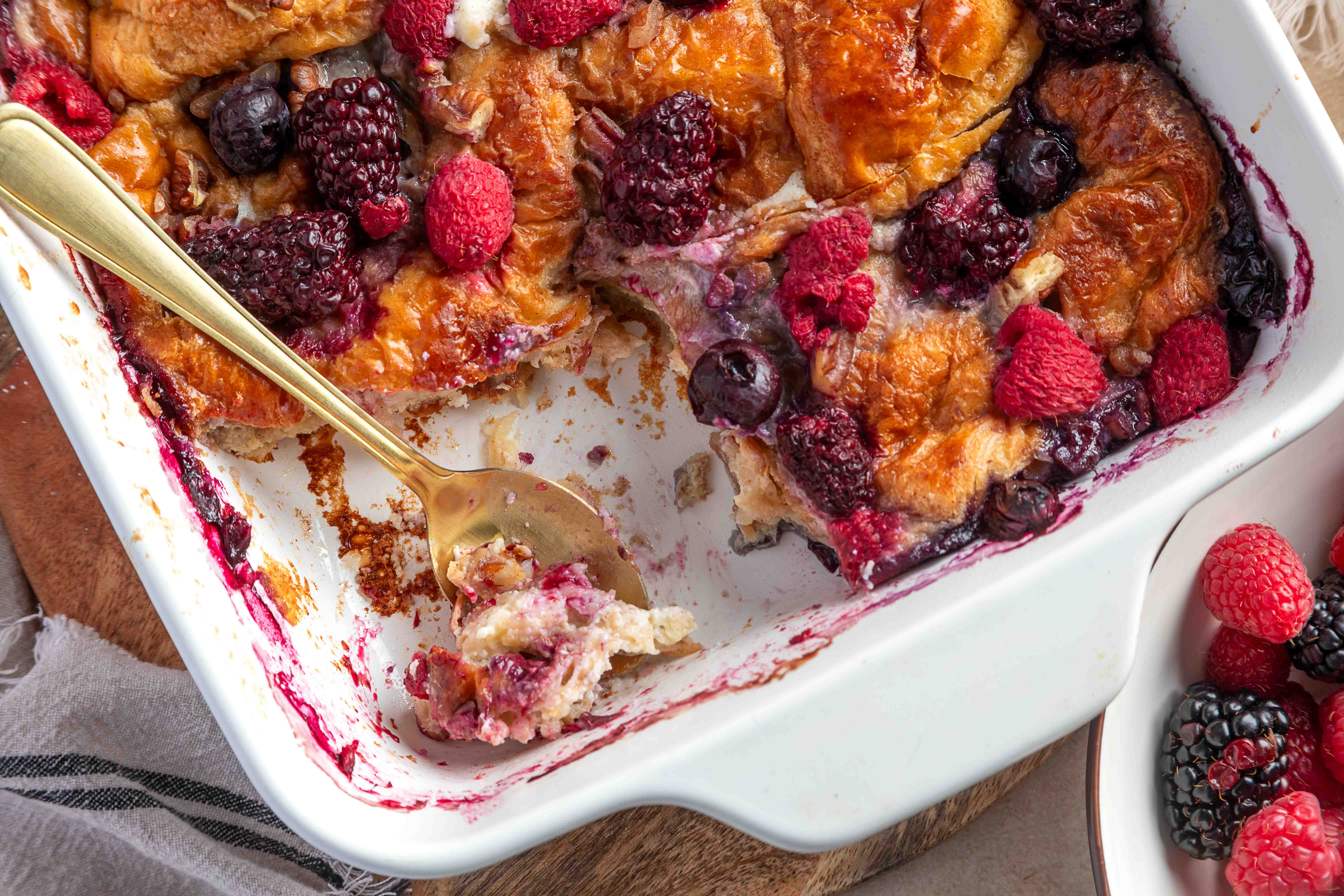 A close-up of a plated slice of croissant French toast casserole showing a creamy cream cheese layer, baked berries, and a lightly crisp top.
