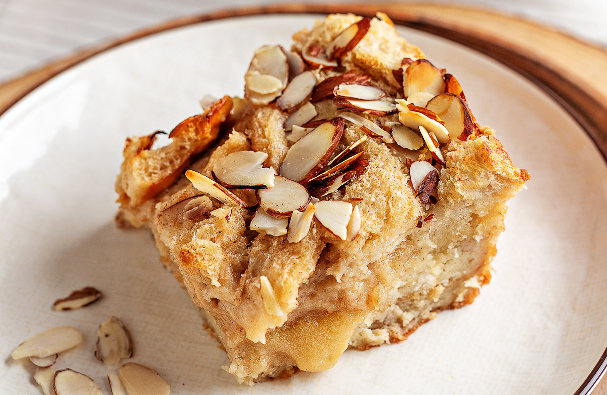 A close-up slice of almond cream bread pudding showing the soft custard interior and toasted sliced almonds on top.