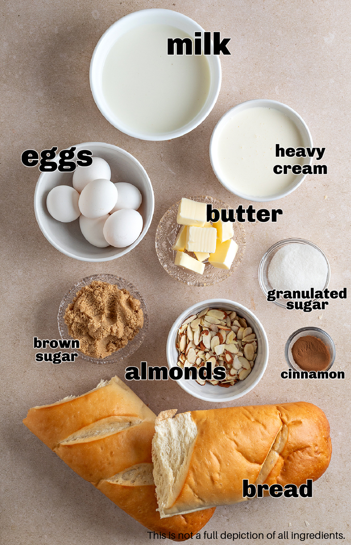 A flat lay of the ingredients for almond cream bread pudding, including milk, cream, eggs, sugars, sliced almonds, butter, cinnamon, and a loaf of bread.