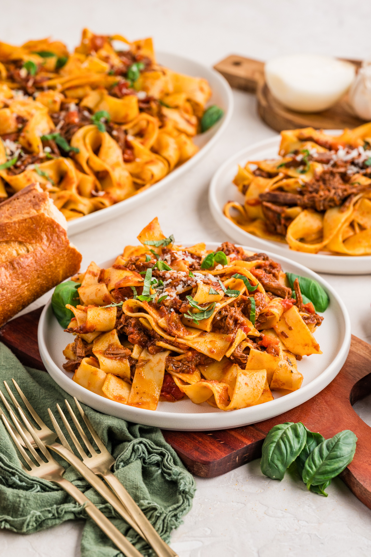 Plates of pappardelle tossed with tender shredded beef rag&ugrave;, served with fresh basil and crusty bread, ready at the table.