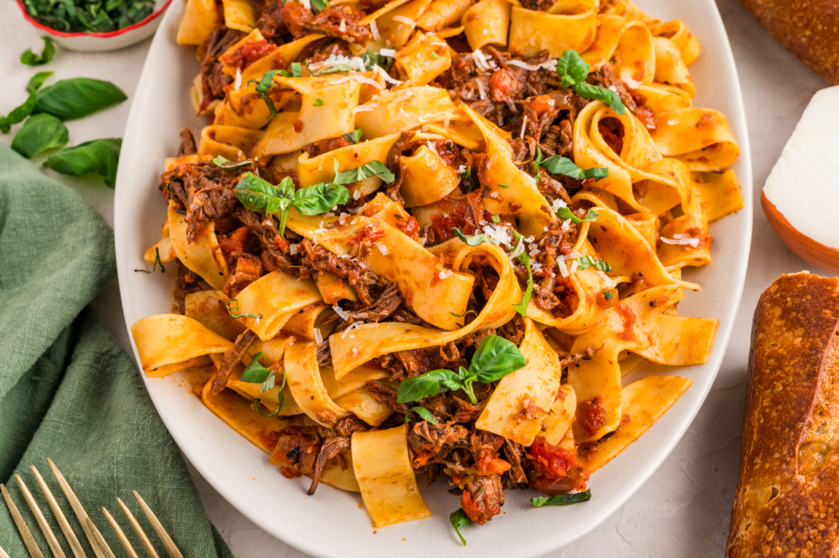 A large oval platter filled with tender beef rag&ugrave; pappardelle, wide noodles twisted with shredded braised beef, tomato-rich sauce, fresh basil, and a sprinkling of parmesan.