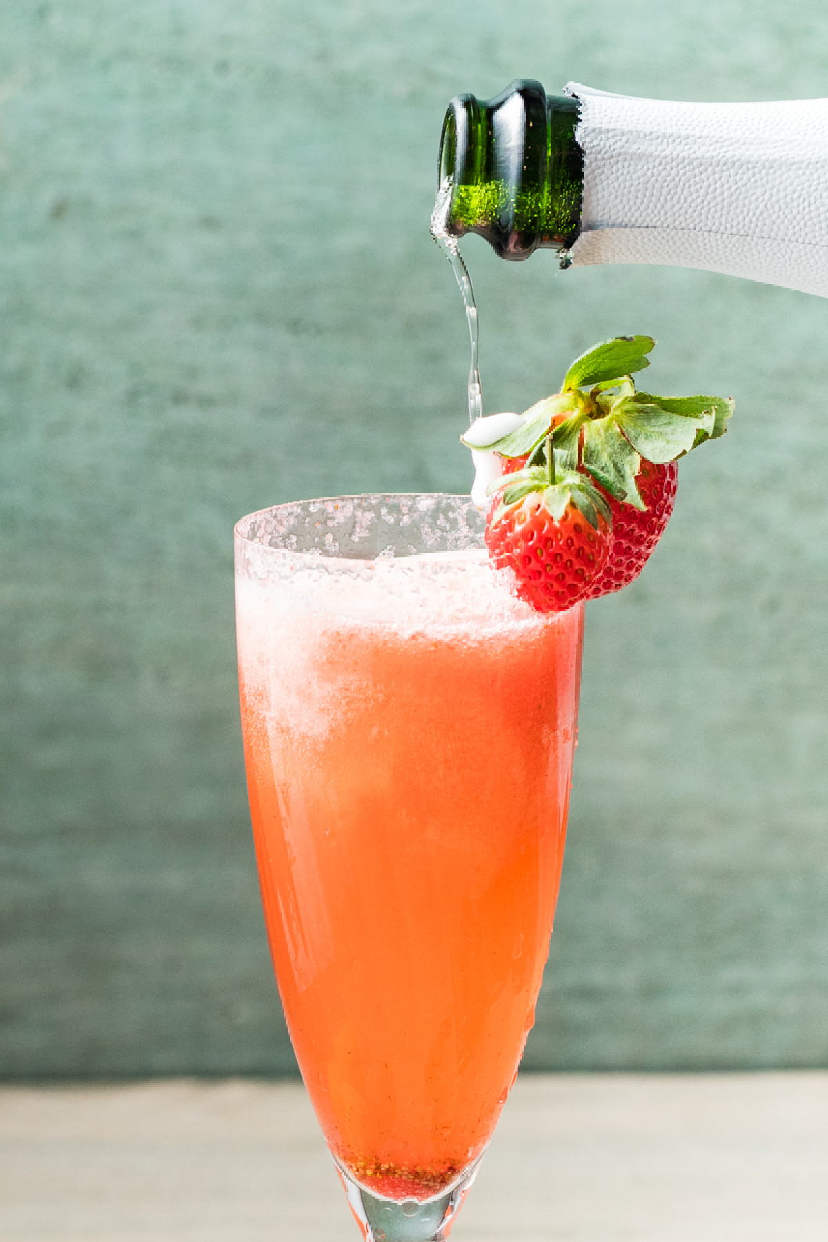 Sparkling wine being poured into a champagne flute filled with strawberry pur&eacute;e.