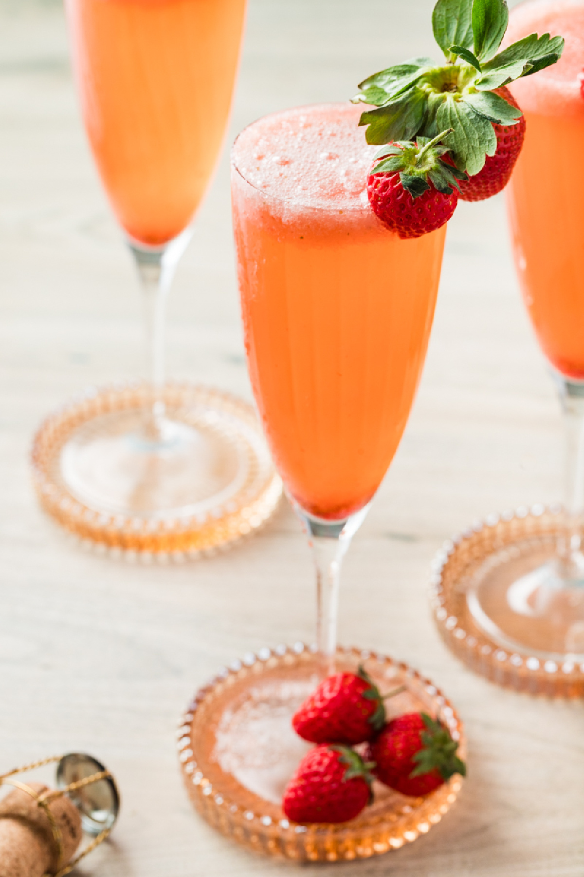 bellini cocktails served in champagne flutes with fresh strawberries on glass coasters.