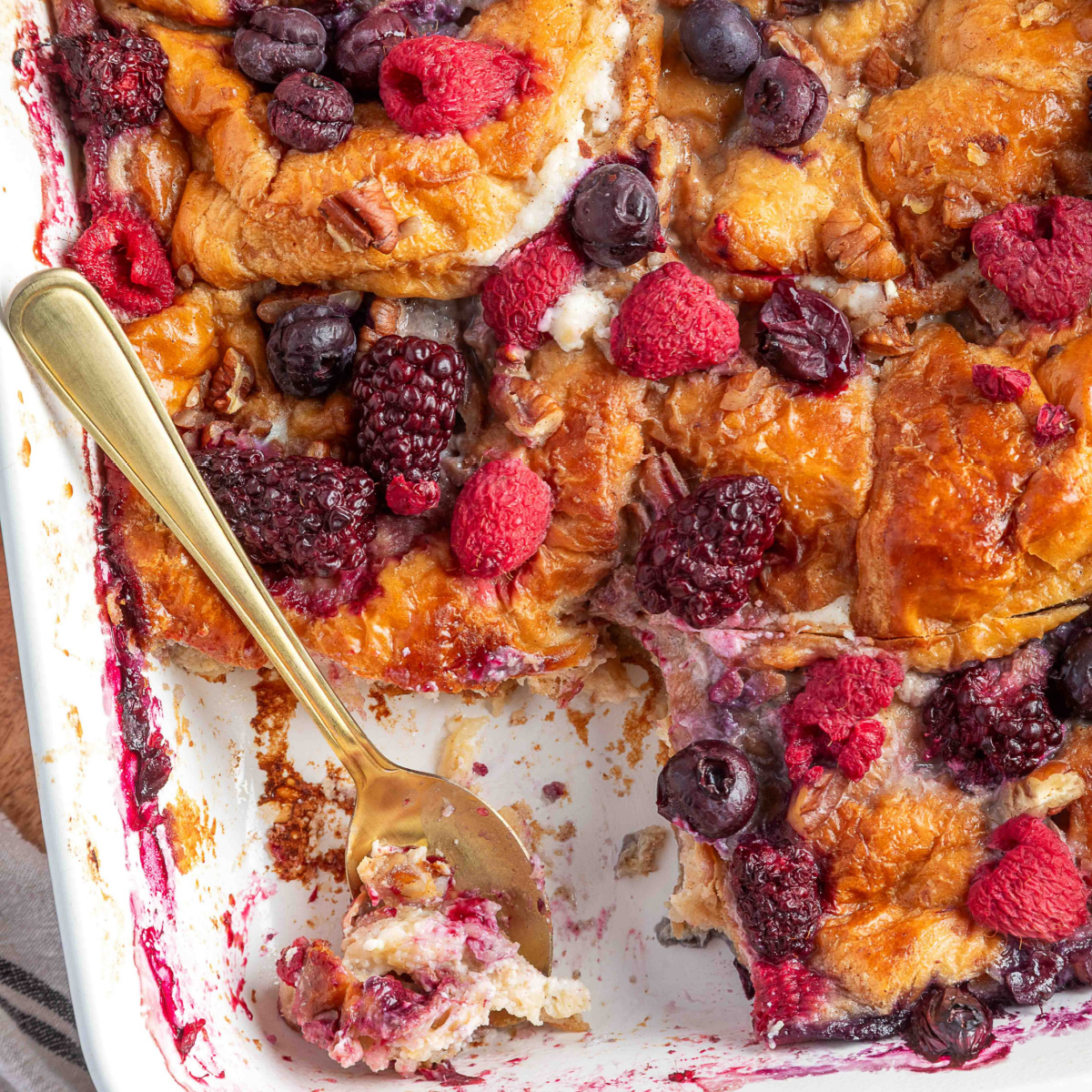 Berry croissant french toast casserole baked with mixed berries and pecans, showing a golden top and custardy interior.
