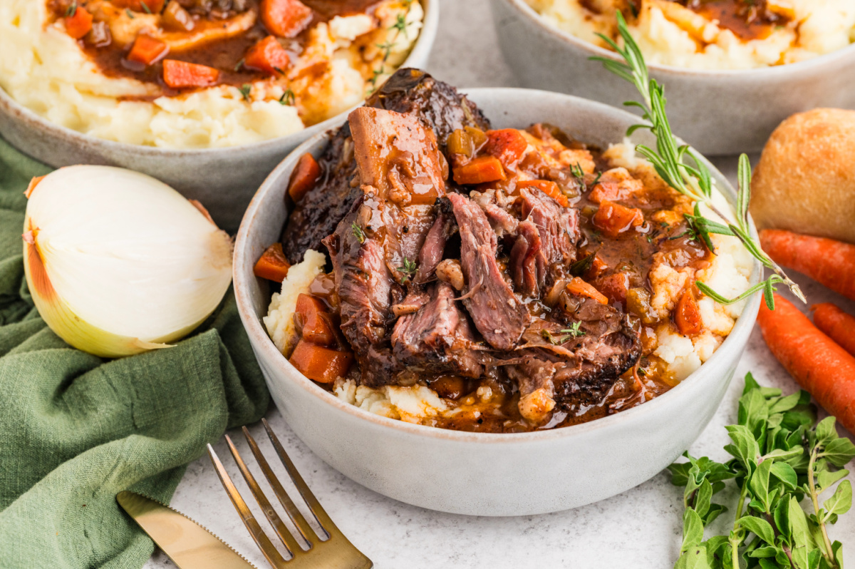 Tender braised short ribs pulled apart over mashed potatoes, surrounded by carrots, herbs, and thickened pan sauce.
