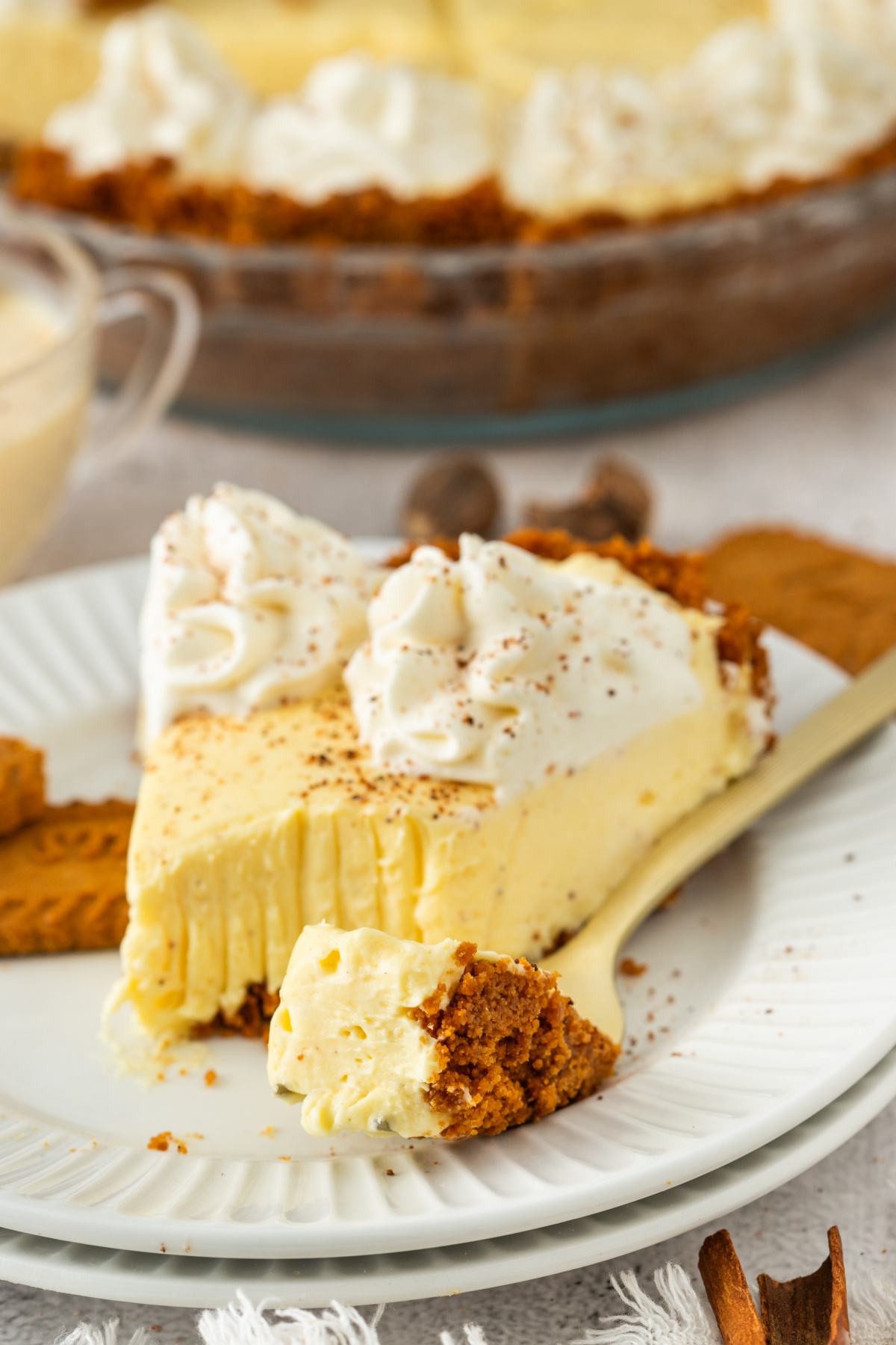 A slice of eggnog cream pie with a forkful taken out, showing the creamy interior and crumbly cookie crust on a white plate.