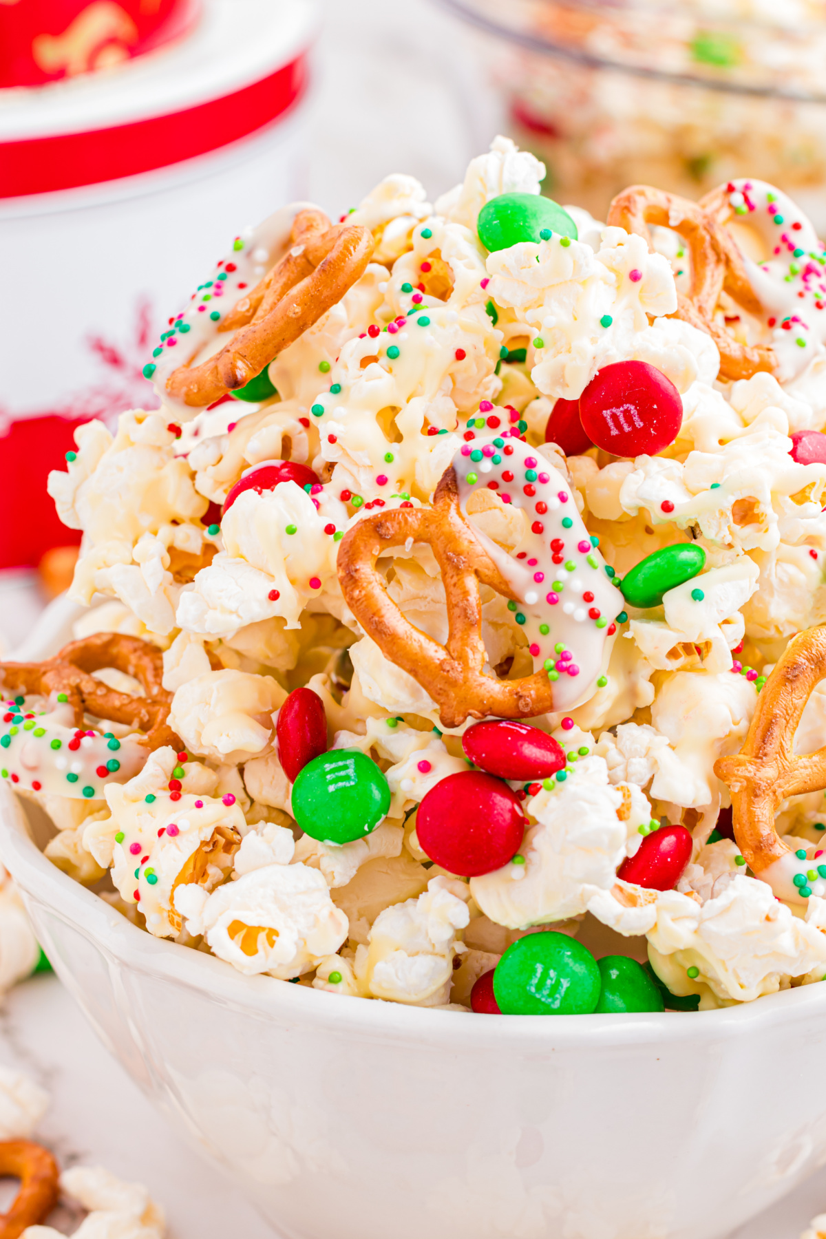 Close-up of Christmas popcorn mix with white chocolate&ndash;coated popcorn, pretzels, holiday sprinkles, and candy-coated chocolates.