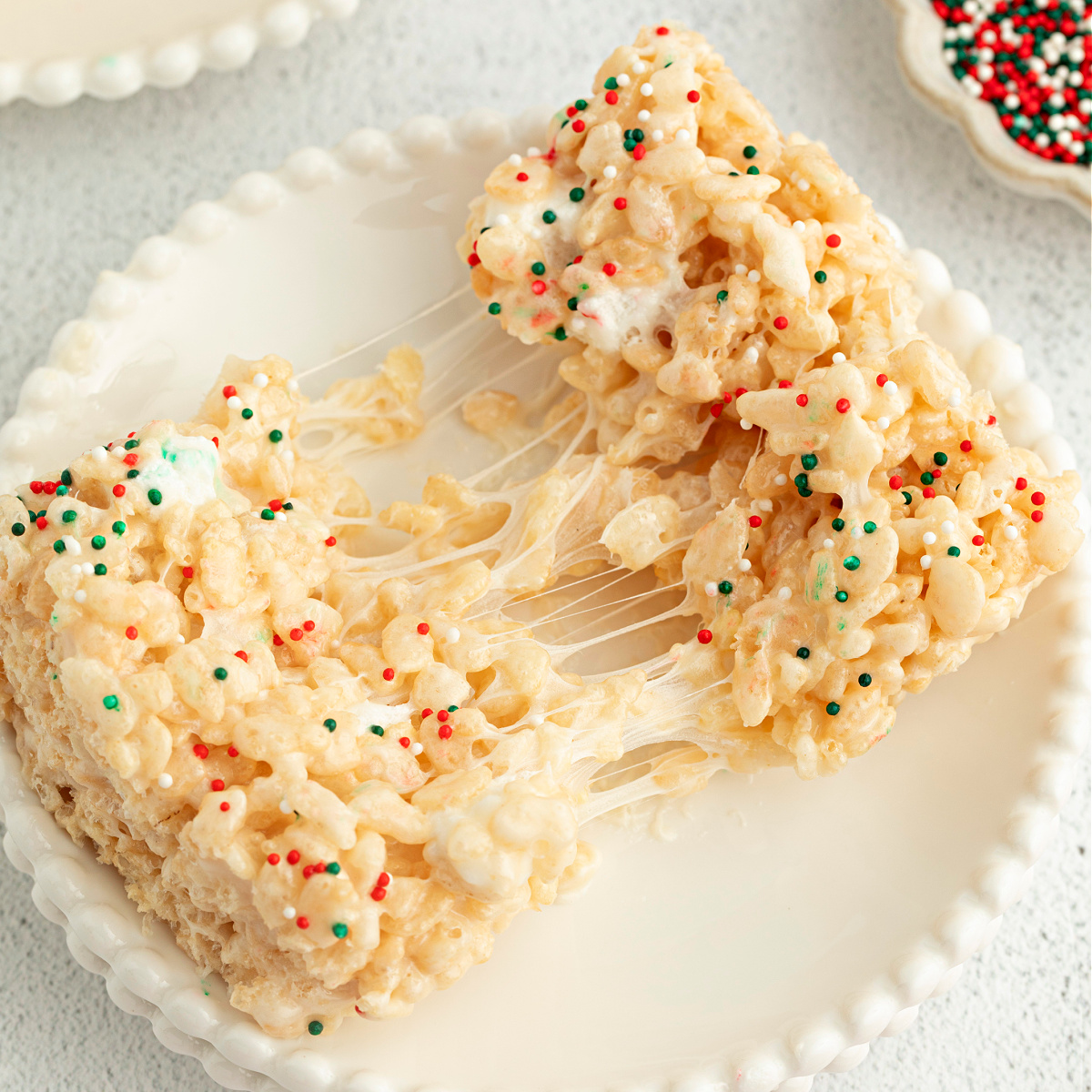 Christmas Sugar Cookie Rice Krispie Treats pulled apart to show gooey marshmallow stretch and festive holiday sprinkles.