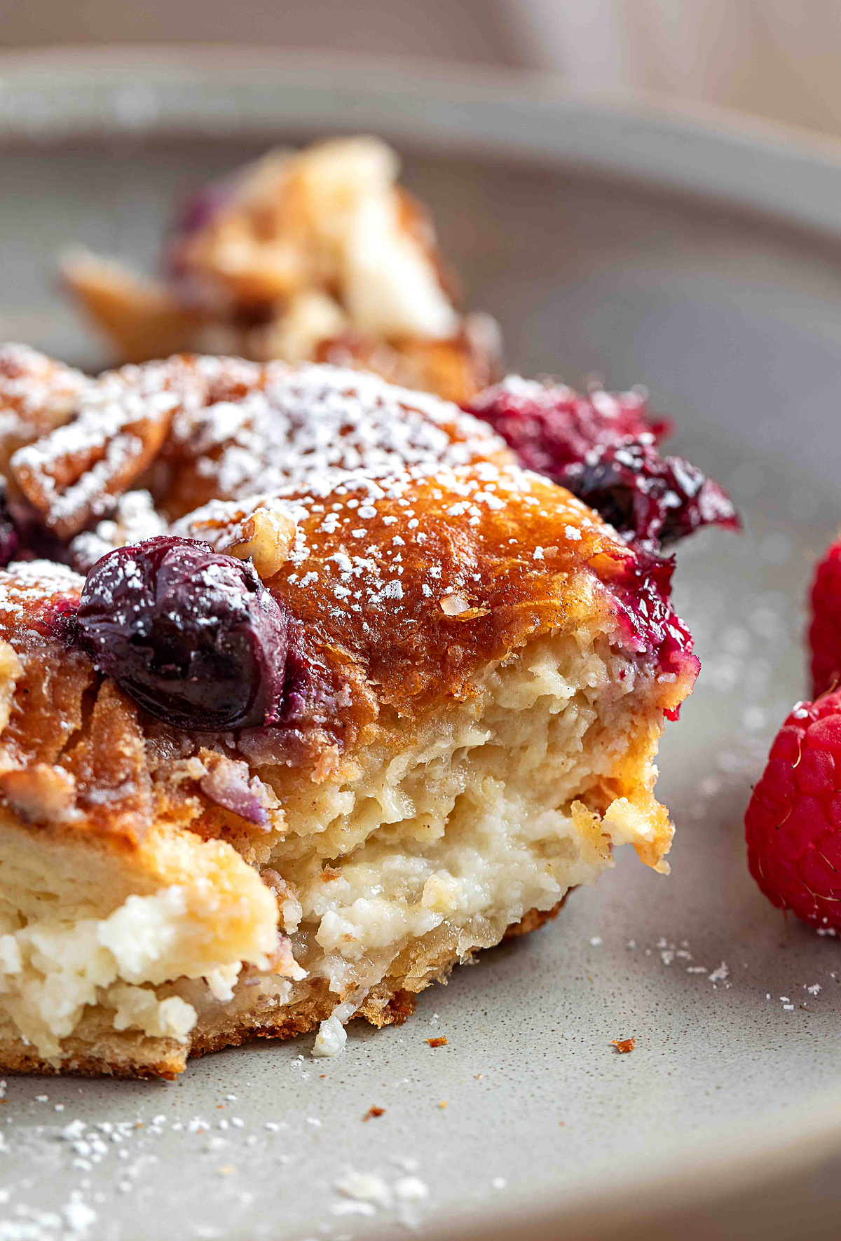 A tight close-up of a sliced croissant French toast casserole showing the thick cream cheese layer, custardy interior, and baked berries on top.