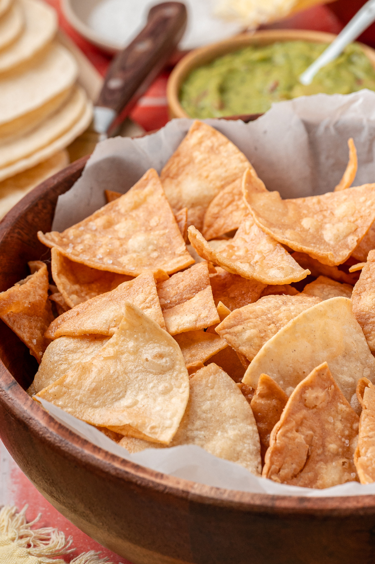 A close-up of golden, blistered corn tortilla chips piled in a wooden bowl, showing crisp edges and light salt clinging to the surface.