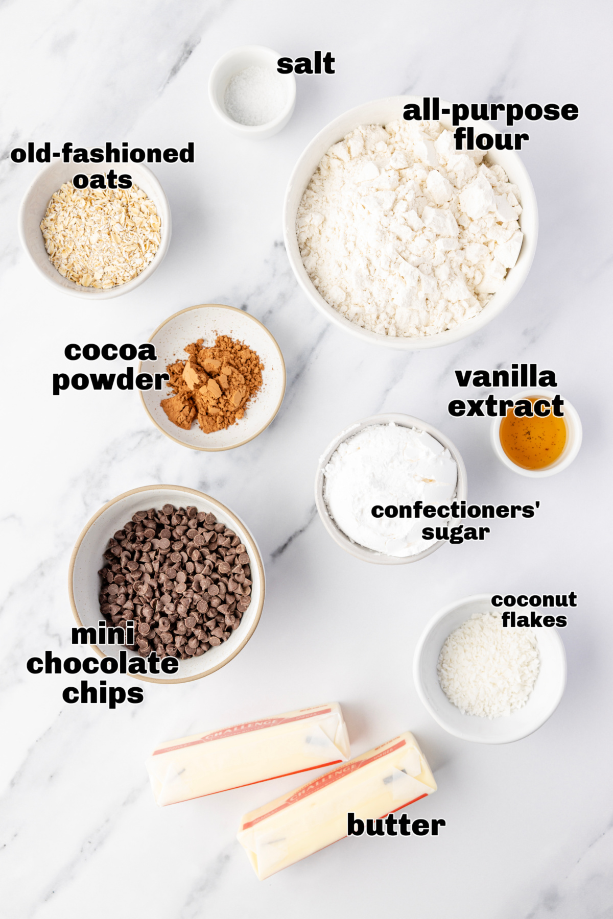 Danish wedding cookies Measured ingredients arranged on a marble surface, including flour, oats, cocoa powder, chocolate chips, butter, and confectioners&rsquo; sugar.