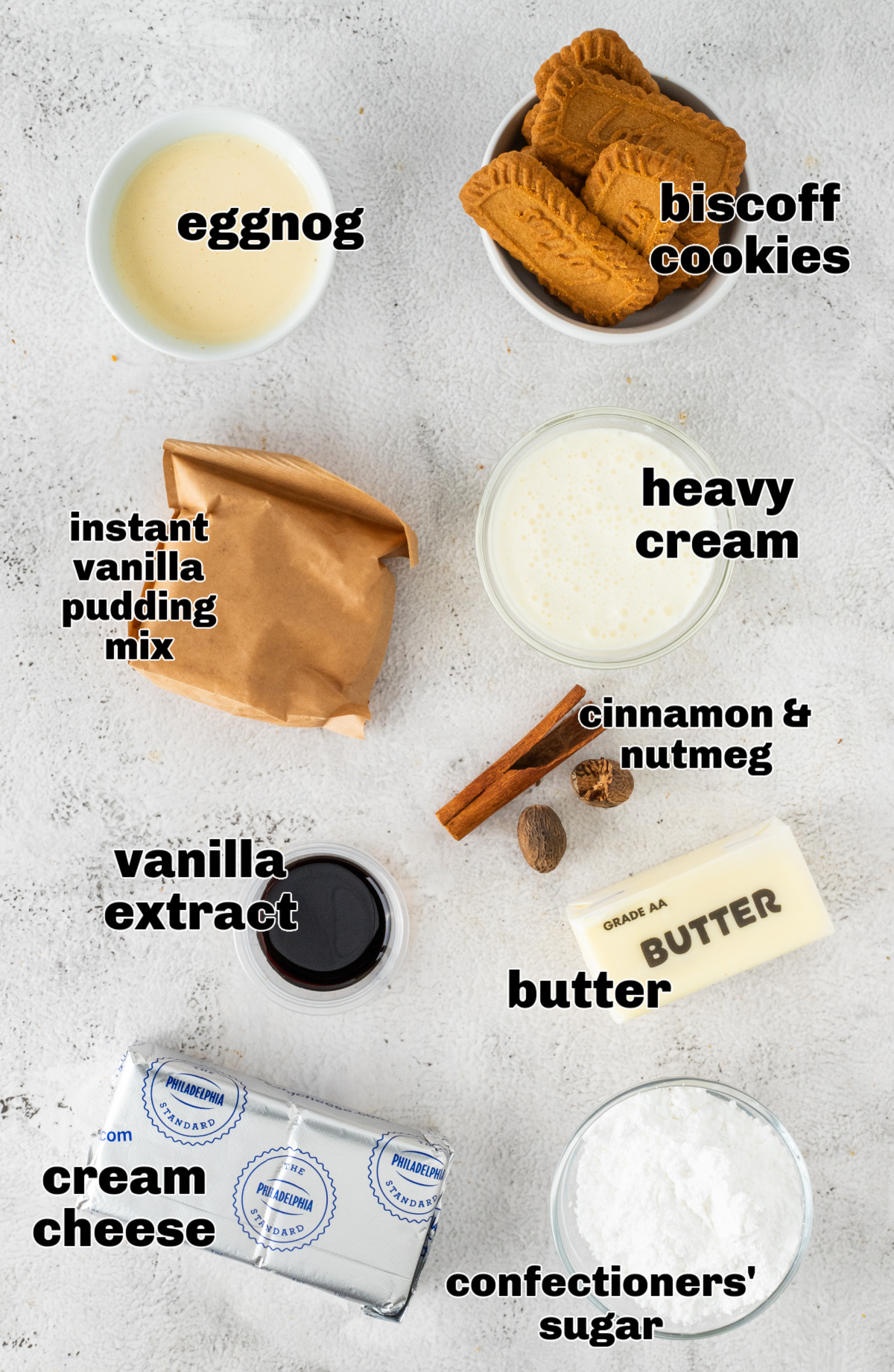 Ingredients for an eggnog cream pie arranged on a light surface, including eggnog, Biscoff cookies, heavy cream, instant vanilla pudding mix, cream cheese, butter, vanilla extract, confectioners&rsquo; sugar, and warm spices.