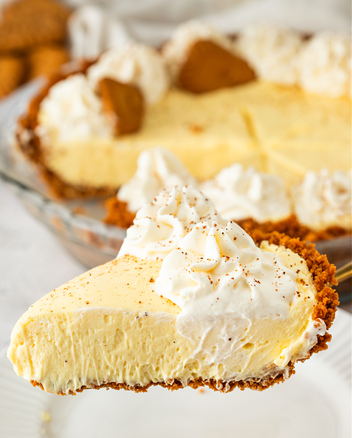 A clean slice of eggnog cream pie lifted from the dish, showing a light, airy filling, a firm cookie crust, and whipped cream on top.