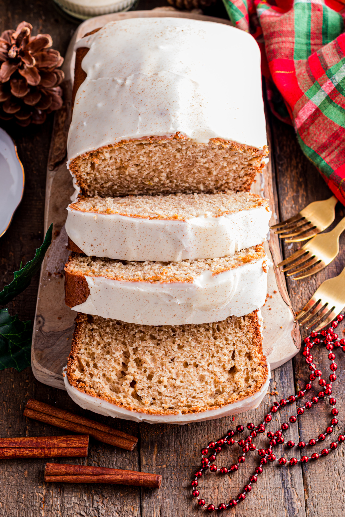 Close-up of eggnog bread with a smooth eggnog glaze dripping over the edge, resting on a wooden board with cinnamon sticks and holiday accents.
