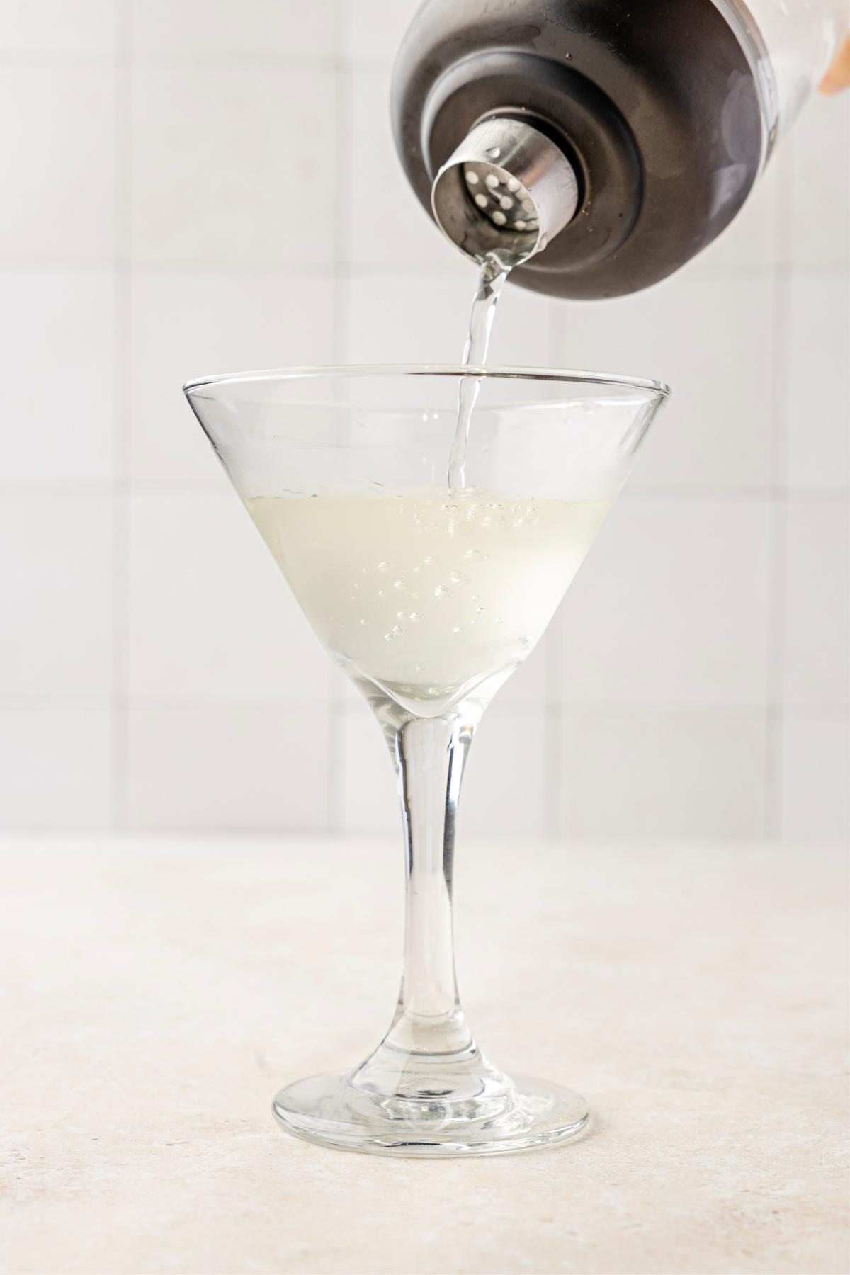 A pale, briny martini being strained from a shaker into a chilled stemmed glass.