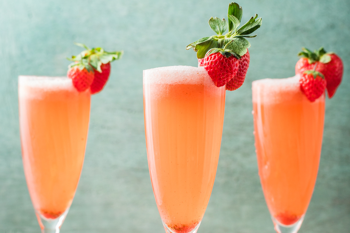 Three champagne flutes filled with pale pink strawberry prosecco cocktails, each garnished with fresh strawberries.