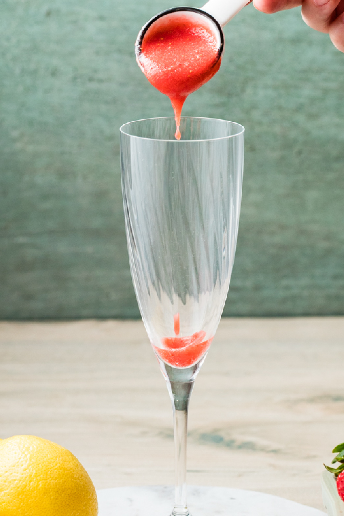 Strawberry pur&eacute;e being spooned into the bottom of a champagne flute.