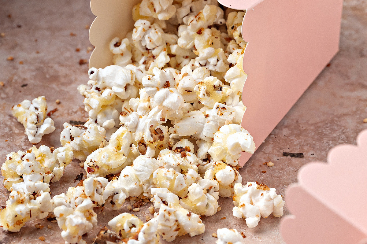 Sweet and spicy furikake popcorn spilling from a pink scalloped treat box, showing the toasted seasoning clinging to each kernel.