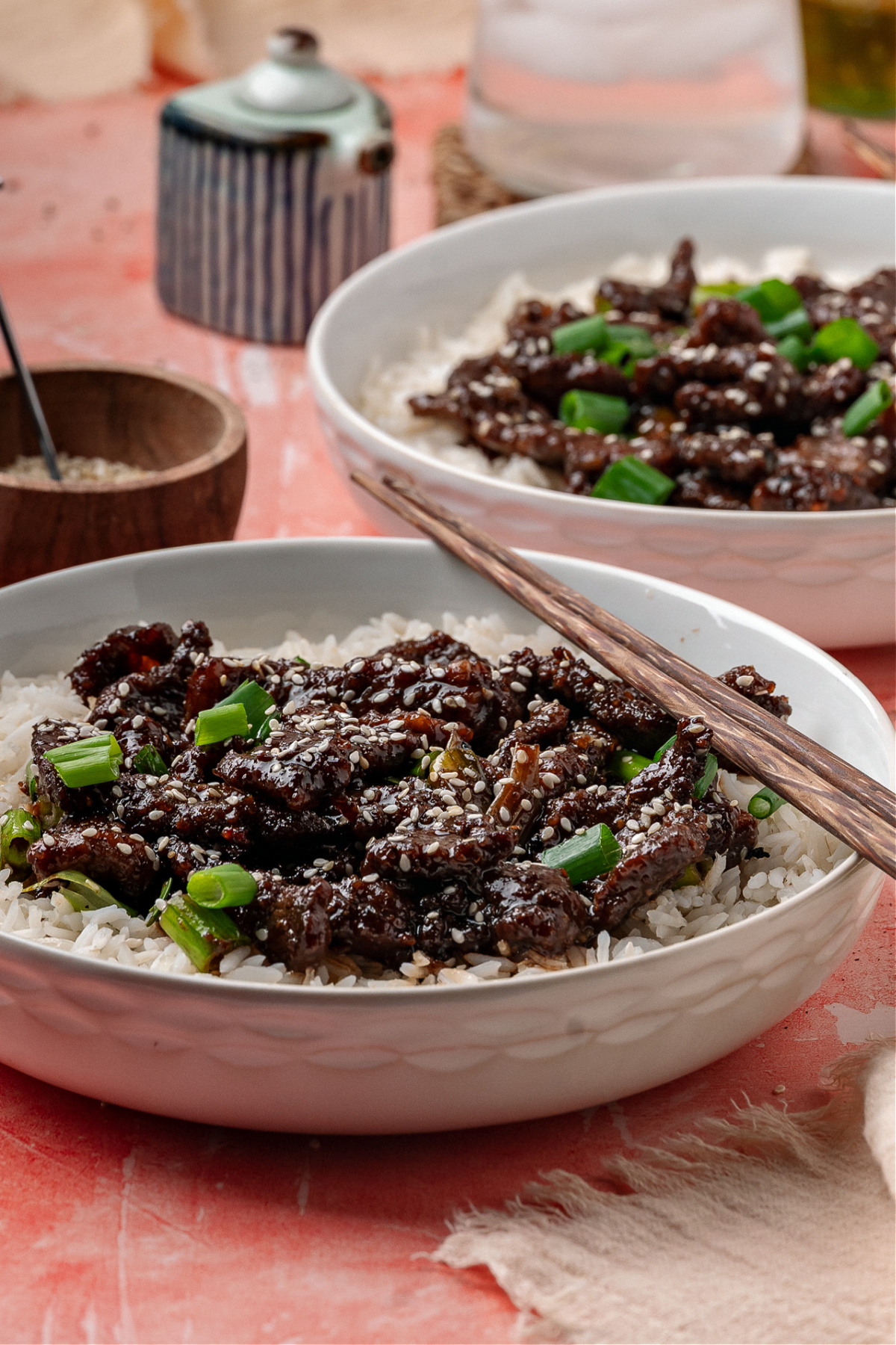 Ginger beef served over white rice with green onions and sesame seeds in a shallow bowl.