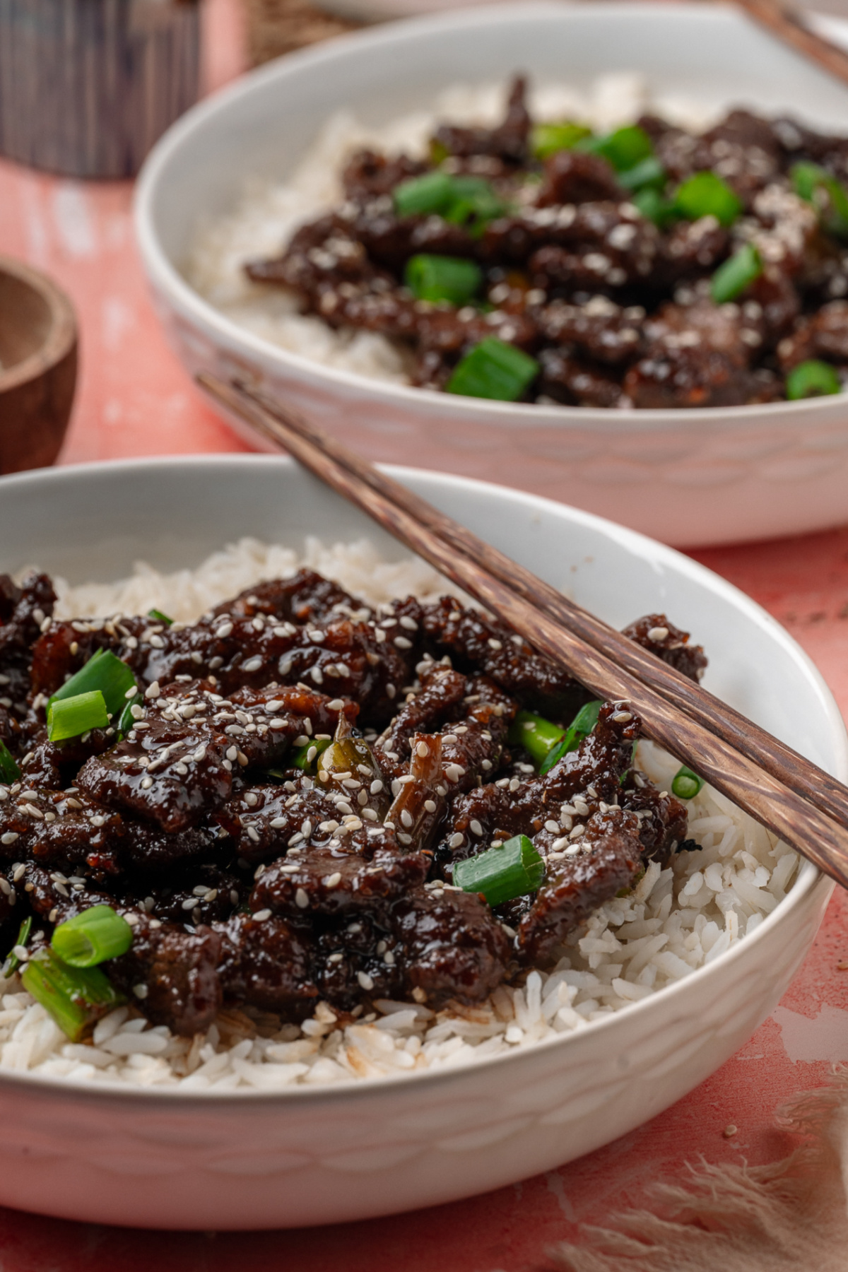 Ginger beef served over white rice with sesame seeds and green onions in a shallow bowl.