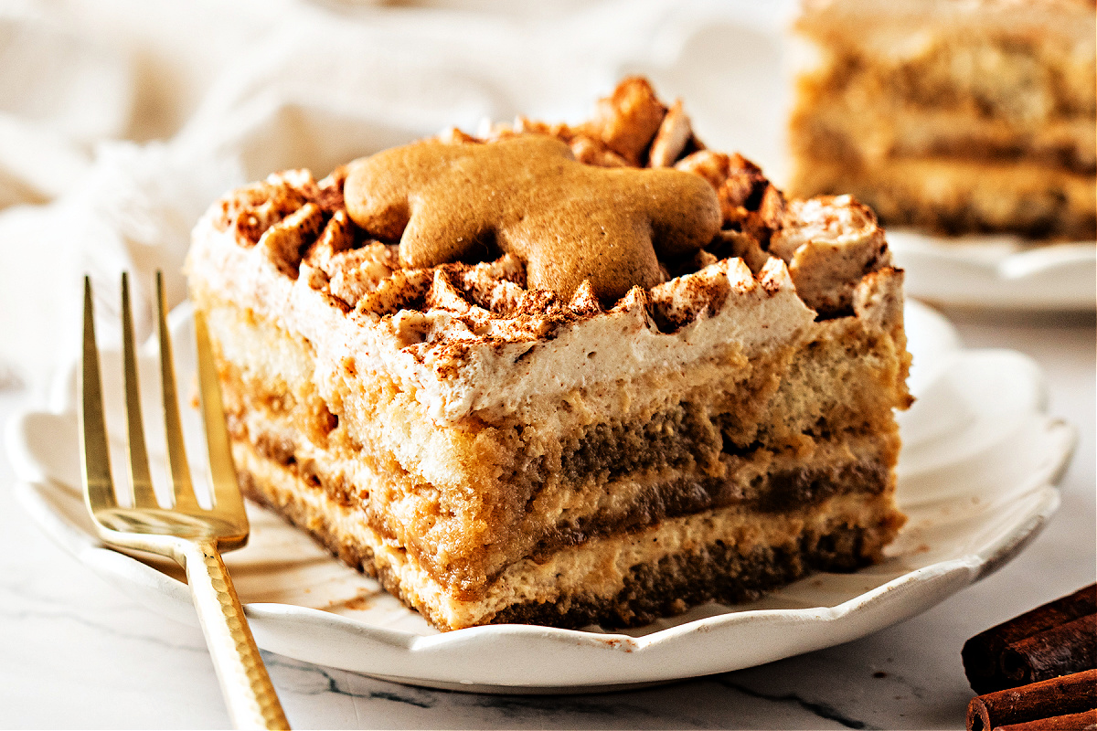 A plated slice of gingerbread tiramisu topped with a small gingerbread cookie, showing the espresso-soaked layers and spiced mascarpone cream with cocoa dusting.