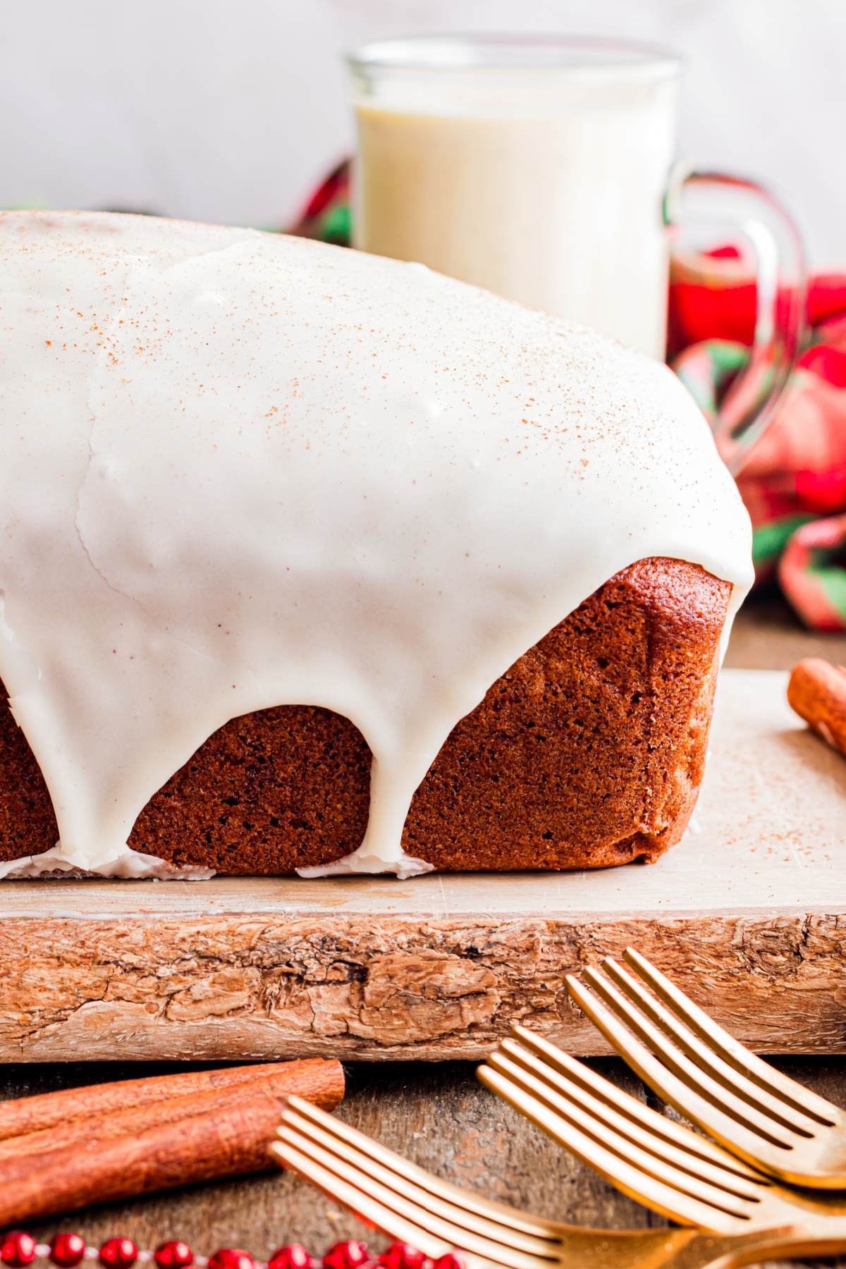 Sliced eggnog bread with a thick eggnog glaze, showing a soft crumb and lightly spiced interior on a wooden board with holiday accents.