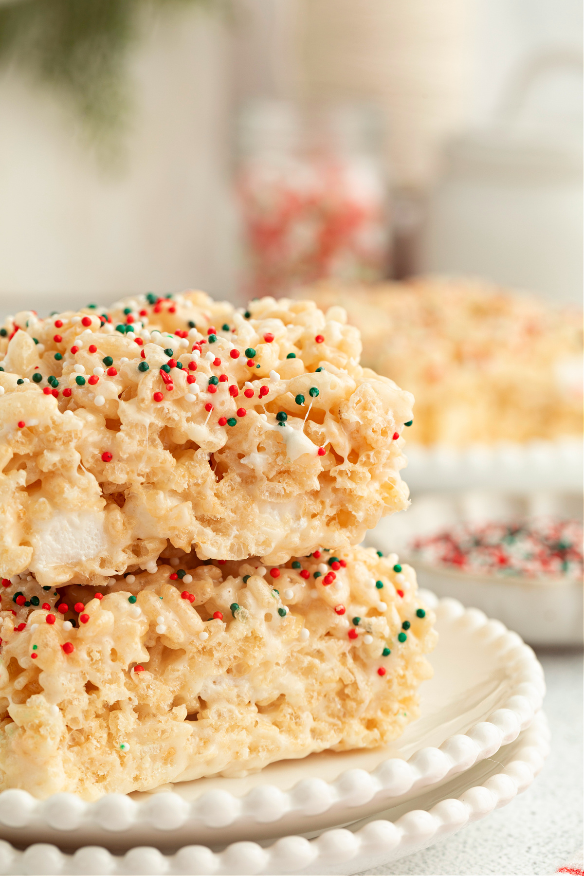 Stacked sugar cookie&ndash;flavored Rice Krispie treats showing a soft marshmallow center and festive red, green, and white sprinkles.