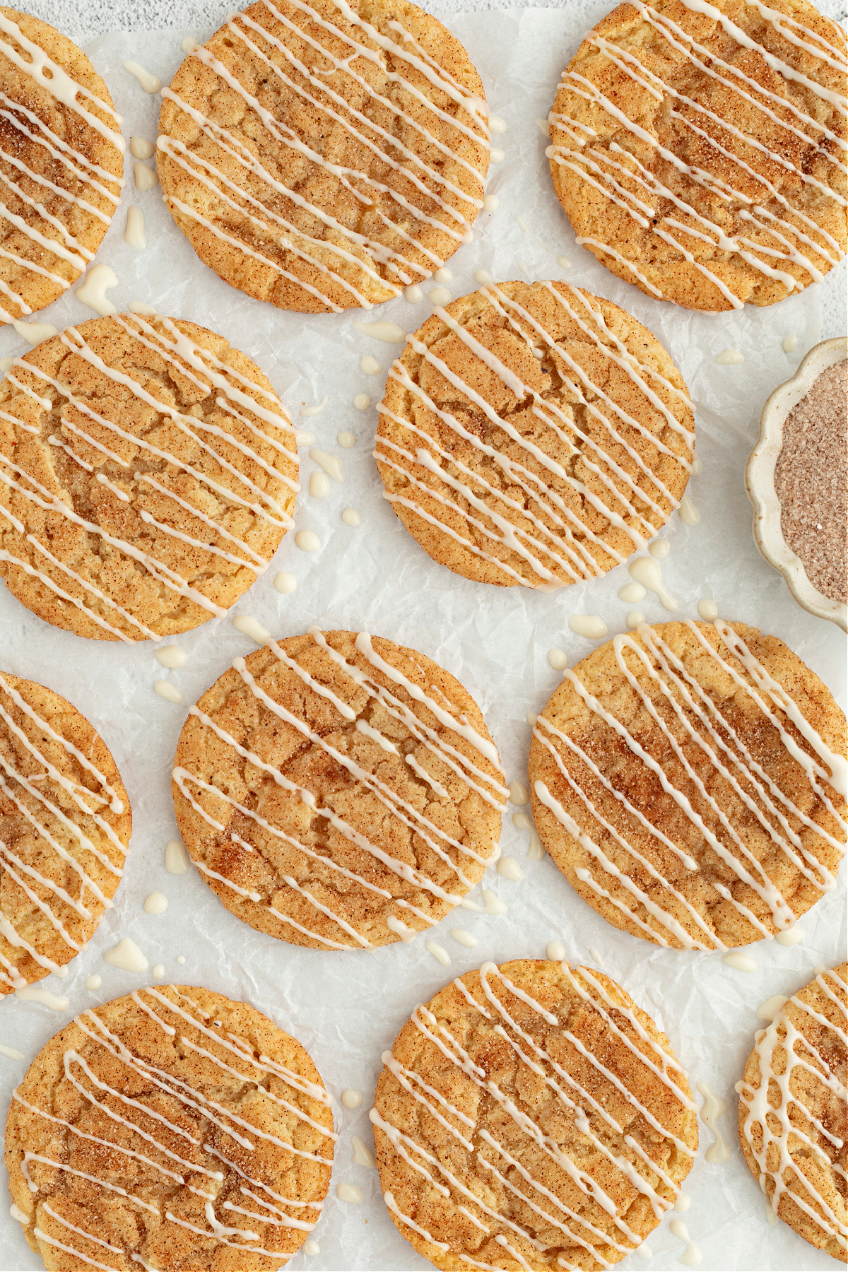 Glazed eggnog snickerdoodles arranged on parchment with cinnamon sugar scattered nearby.
