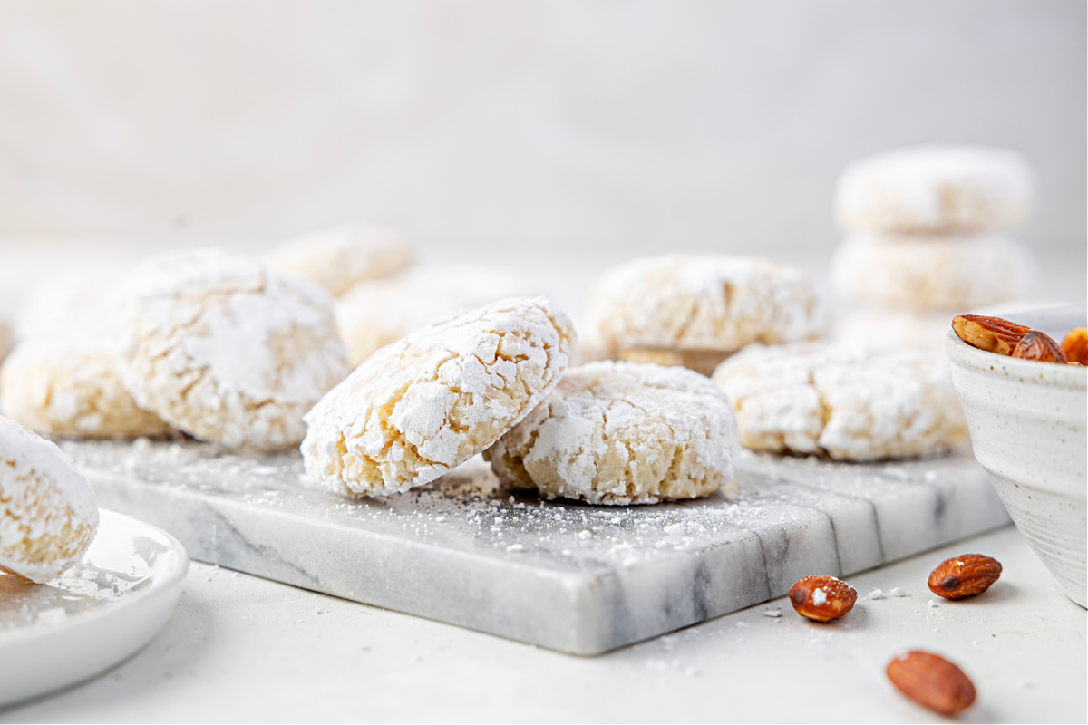 Powdered almond cookies with a soft, crackled finish arranged on a marble board in bright winter light.